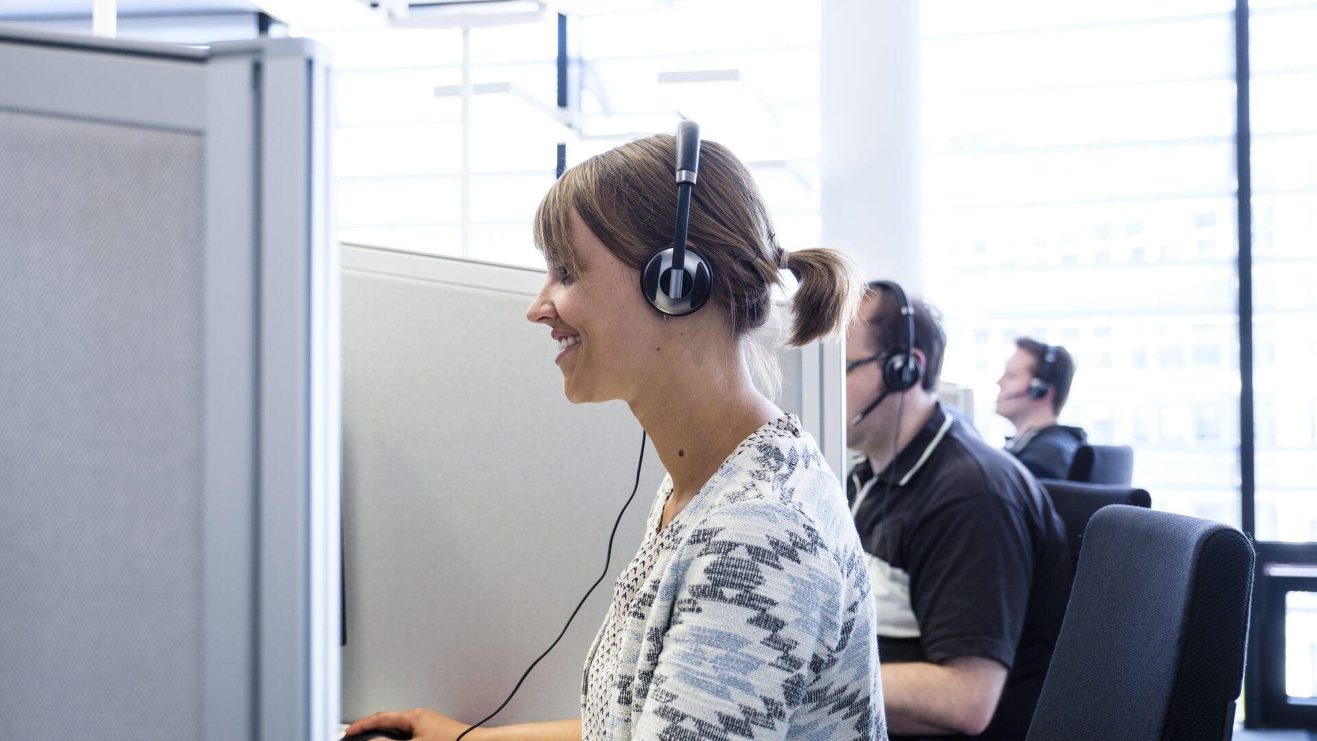 Mehrere Personen mit Headsets arbeiten in einem modernen Großraumbüro an Computern.