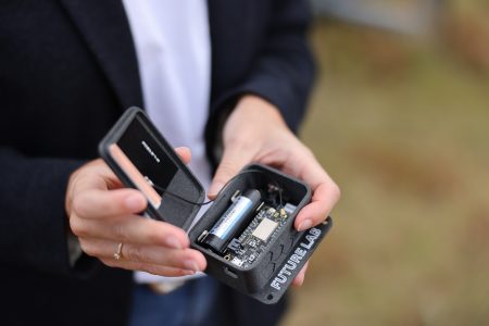 Eine Person hält ein kleines, geöffnetes Gerät mit der Aufschrift "Future Lab" in den Händen. Das Gerät enthält eine Batterie und elektronische Komponenten.