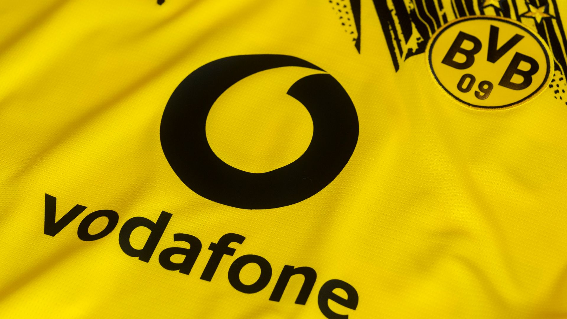 Nahaufnahme eines gelben Fußballtrikots mit schwarzem „vodafone“-Logo und BVB 09-Vereinswappen von Borussia Dortmund auf der Brust.