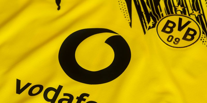 Nahaufnahme eines gelben Fußballtrikots mit schwarzem „vodafone“-Logo und BVB 09-Vereinswappen von Borussia Dortmund auf der Brust.