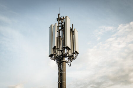 Ein Mobilfunkmast mit mehreren Antennen ragt in den Himmel, umgeben von einigen Wolken. 