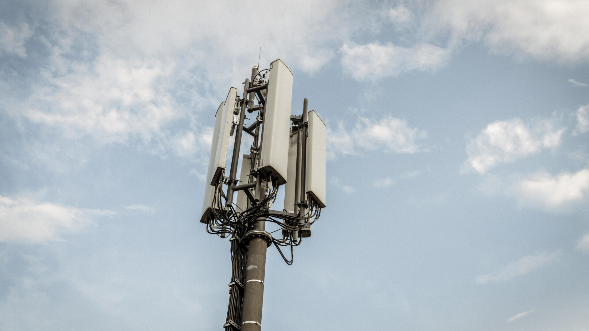 Ein Mobilfunkmast mit mehreren Antennen ragt in den Himmel, umgeben von einigen Wolken.