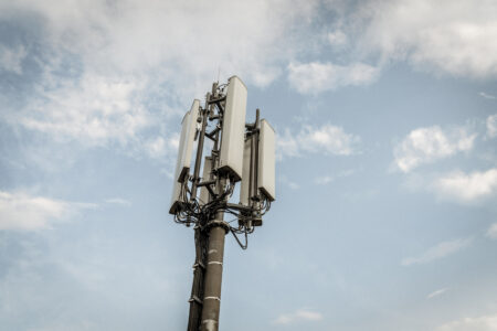 Ein Mobilfunkmast mit mehreren Antennen ragt in den Himmel, umgeben von einigen Wolken.