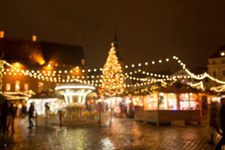 Verschwommene Ansicht eines festlich beleuchteten Weihnachtsmarktes mit Lichterketten, einem geschmückten Weihnachtsbaum und einem Karussell.